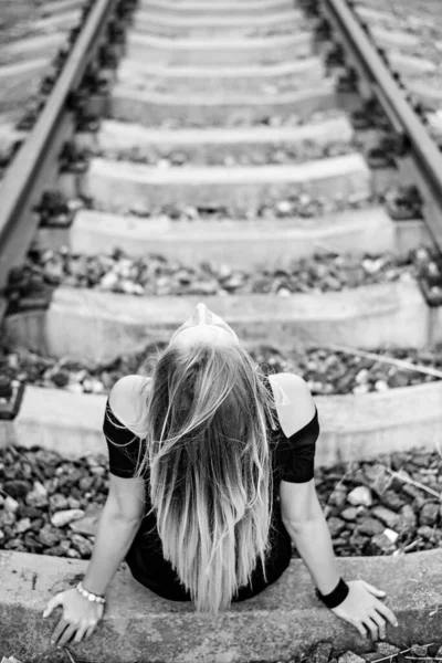 長い脚を持つ黒い短いドレスに長い髪のブロンドを持つ悲しいと孤独な女の子は 鉄道線路のレールに座っています 愛する人と別れた後の損失 壊れた心 失望の痛み — ストック写真
