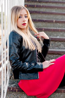 Güzel, modern, modaya uygun, uzun saçlı, kırmızı rujlu sarışın bir kız merdivenlerde oturuyor. Etek, siyah deri ceket, çizme ve tayt giymişti. Genç anne. Formda, saygıdeğer bir yüz.