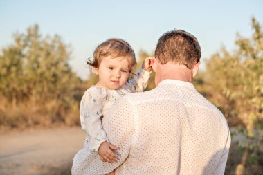 Genç kızıl saçlı bir adam küçük güzel bir kızı kollarında tutuyor. Omuzlarında yuvarlar, oynar, sallar, el ele tutuşur. Bebek iki dişiyle gülüyor. Ebeveynlik kavramı, çocuk bakımı
