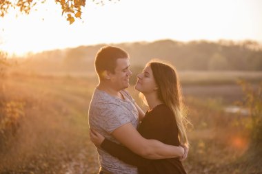 Genç bir adam uzun saçlı, gülümseyen güzel bir sarışını öpüyor. Sonbahar ormanının arka planına sarılan bir çiftin yakın plan portresi. Mutlu aşıklar birlikte seyahat eder.