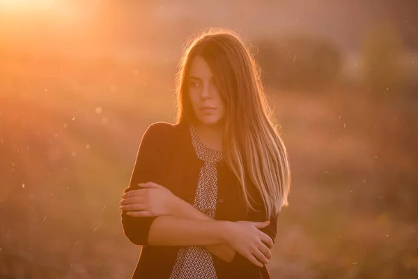 現代的で美しい少女は バーガンディのジャケット 暗いジーンズで 日没時の秋のフィールドの背景に風になびくブロンドの髪のフィールドに立っています 秋の旅行 街からの休息 思考の自由 — ストック写真