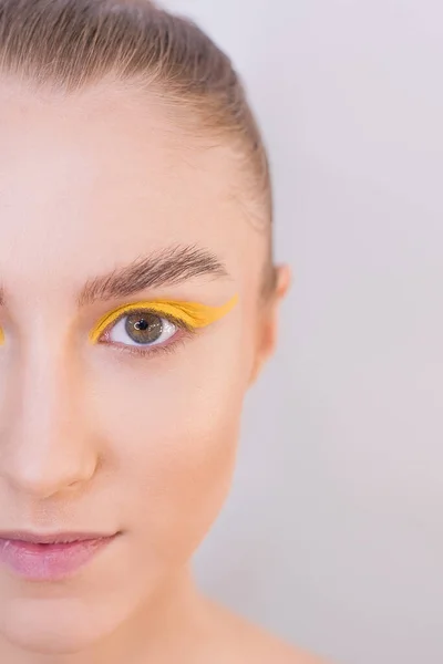 Step-by-step instructions on how to make a bright art makeup for a butterfly at home. DIY Step 3. Even out skin tone, apply yellow eyeshadow on the upper eyelid, make the skin shine. Close up portrait