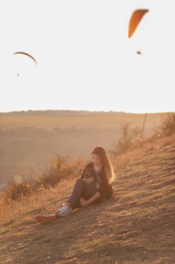 Modern bir kız Schnauzer ile sonbahar tepelerinde yürüyor. Yanmış çimenlerin üzerinde oturuyor, sevgiyle köpeğe sarılıyor, gün batımına özen gösteriyor, gülümsüyor, kameraya bakıyor, paraşütçüler arkasından uçuyor. Gezgin hayvan.