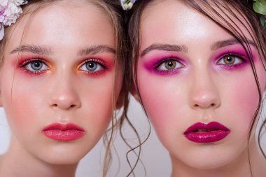 Parlak ve moda bahar sanatları iki güzel kız kardeş için profesyonel makyaj. Portreyi kapat. Taze bahar çiçeklerinden oluşan bir halka kafalarda şakayık. Temiz ciltli, yüz bakımlı bir model. Gençler için kozmetoloji