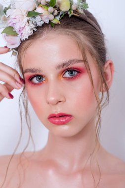 Çıplak moda parlak makyajlı genç bir kızın ekstra yakın plan portresi, saç stili, taze çiçeklerden yapılmış bir halka: piyonlar, tarla çiçekleri, okaliptüs, ranunculus. Temiz cilt. Nedime