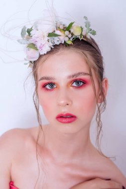 Çıplak moda parlak makyajlı genç bir kızın ekstra yakın plan portresi, saç stili, taze çiçeklerden yapılmış bir halka: piyonlar, tarla çiçekleri, okaliptüs, ranunculus. Temiz cilt. Nedime