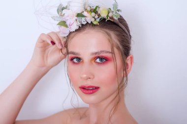 Çıplak moda parlak makyajlı genç bir kızın ekstra yakın plan portresi, saç stili, taze çiçeklerden yapılmış bir halka: piyonlar, tarla çiçekleri, okaliptüs, ranunculus. Temiz cilt. Nedime