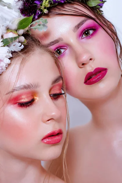 Parlak ve moda bahar sanatları iki güzel kız kardeş için profesyonel makyaj. Portreyi kapat. Taze bahar çiçeklerinden oluşan bir halka kafalarda şakayık. Temiz ciltli, yüz bakımlı bir model. Gençler için kozmetoloji