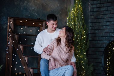 Birbirine aşık mutlu çift, ağaçlardan ve ışıklardan yapılmış çelenklerle süslenmiş el yapımı ahşap bir merdivende oturuyor. Genç bir adam güzel bir kıvırcık kızı arkadan kucaklıyor, gülüyorlar, öpüşüyorlar Noel beklentisiyle.