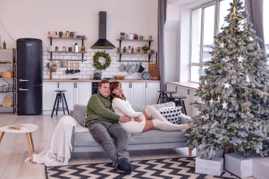 Sıcak örülü kazak giyen sevgi dolu bir çift sarılıp öpüşüyor. Sevgililer evde yeni yılı kutlar, beyaz mutfakta Noel ağacının yanında oturur, el ele tutuşur, birbirlerine bakarlar. Portreyi kapat, boşluğu kopyala