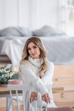 Güzel kıvırcık saçlı, uzun saçlı, Noel ağaçlarının yanında ışık çelenkleriyle. Gri örgü süveter ve büyük yakalı beyaz gülüşlü bir kızın yakın plan portresi. Boşluğu, dokuyu kopyala