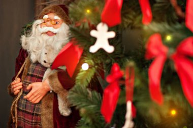 Yılbaşı kartı. Noel ağacı kırmızı büyük fiyonklarla süslenmiş, ipteki beyaz zencefilli çörekler, arka plan parlak bokeh ile bulanıklaşmış. Noel Baba heykelciği. Uzayı kopyala Şenlikli 