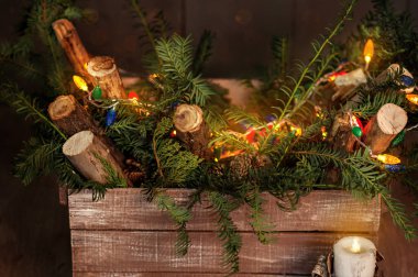 Noel dekorasyonlarının yeni yıl kartı. Ahşap bir şömine dizaynı. Kutu taze köknar ağacı iğneleriyle dolu, parlak çelenklerle süslenmiş, yazıtlar Xmas, rustik tarzı mumlar. Boşluğu kopyala