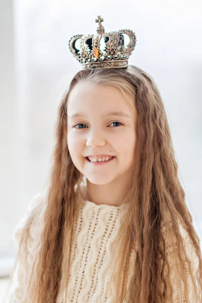 一个金发小女孩的特写画像 她穿着一件白色针织毛衣 头上戴着一顶皇冠 她笑着看着镜头 白雪公主儿童冬季嘉年华服装 圣诞佳节 — 图库照片