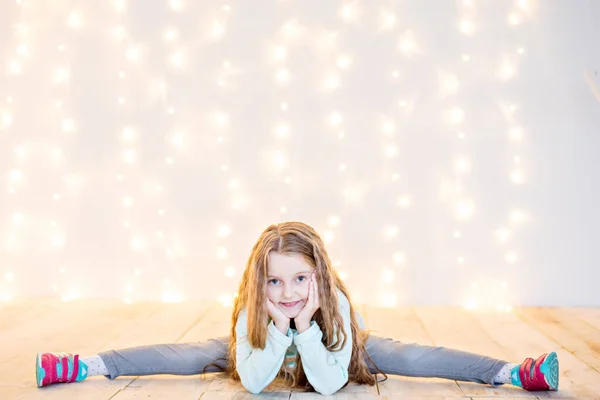 一个漂亮的金发小女孩坐在木地板上 背景是模糊的黄色圣诞花环 新年贺卡 Toddler运动 复制空间 节日质感 — 图库照片