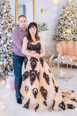 Noel İçi 'nin arka planında şık giyinmiş orta yaşlı bir çift: karla kaplı ağaçlar, beyaz şömine, lüks mobilyalar. Ayyaş bir kadın, akşam giysisi ışıkların arasında.