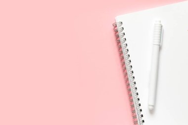 Okula dönelim. Beyaz bir deftere sarmalı beyaz bir kalem. Hassas pembe bir arkaplan üzerinde metin için yer alan düzen ve düz uzanma.