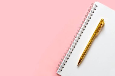 Altın kalem ve sarmalı beyaz defter. Hassas pembe bir arka planda metin için yer alan düz ve düz bir düzen. Okula dönüş kavramı.