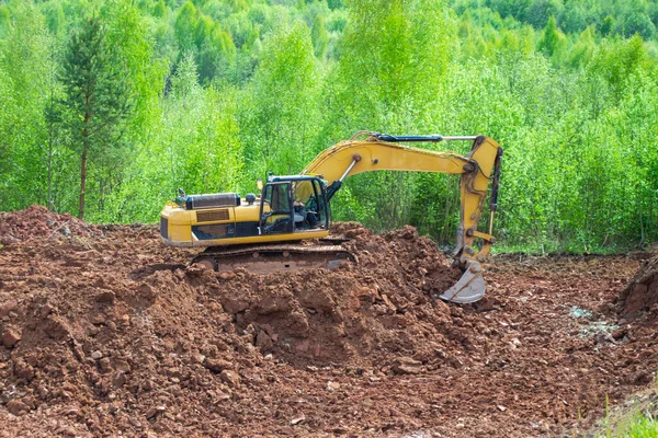 The yellow excavator digs red clay with a large bucket. Clay mining.
