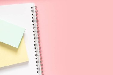Üzerinde spiral ve iki renkli çıkartma olan beyaz bir defter. Hassas pembe bir arka planda metin için yer alan düz ve düz bir düzen. Okula dönüş kavramı.