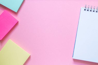 Düzen ve düz metin için yer. Hassas pembe arka planda üç renkli çıkartma ve spiral şeklinde beyaz bir defter. Okula dönüş kavramı.