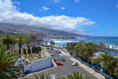 Nisan 2018, Puerto de la Cruz, Kanarya Adaları, İspanya. Şehir, büyük dalgalı sahil, palmiye ağaçları ve arabalı bir yol.. 