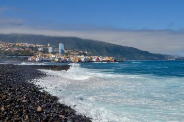 Siyah volkanik kum ve büyük dalgalar. Şehir, sahil ve Teide volkanı dağları. Puerto de la Cruz, Kanarya Adaları. İspanya.