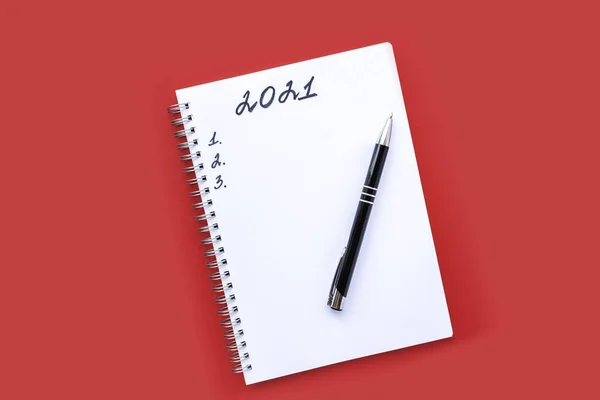 Anteckningsbok med en spiral och svart penna på en röd bakgrund. Planeringslista och nummer 1, 2 och 3. Inskriptionen 2021. — Stockfoto