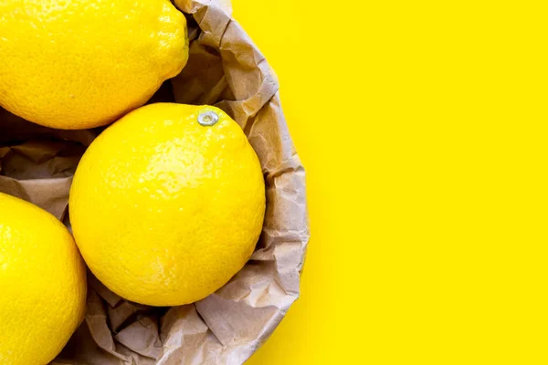 Három élénk citrom közelkép sárga háttérrel. Friss citrom csoport újrahasznosított papírzacskóban. — Stock Fotó