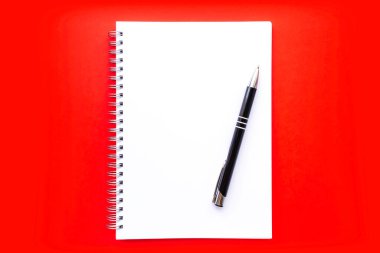 Kalemle sarmalı boş beyaz defter kağıdı. Düz kırmızı arka plan. Yeni yıl, Noel ya da Sevgililer Günü kavramı. Düzen, düz yatak ya da maket. Boşluğu kopyala, metin için yer.