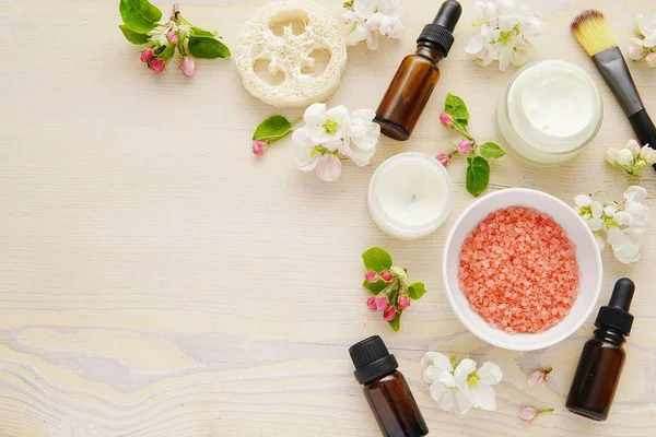 Spa, skin care products composition on wooden background with flowers, sea salt, cosmetic oils, facial creme, flat lay.