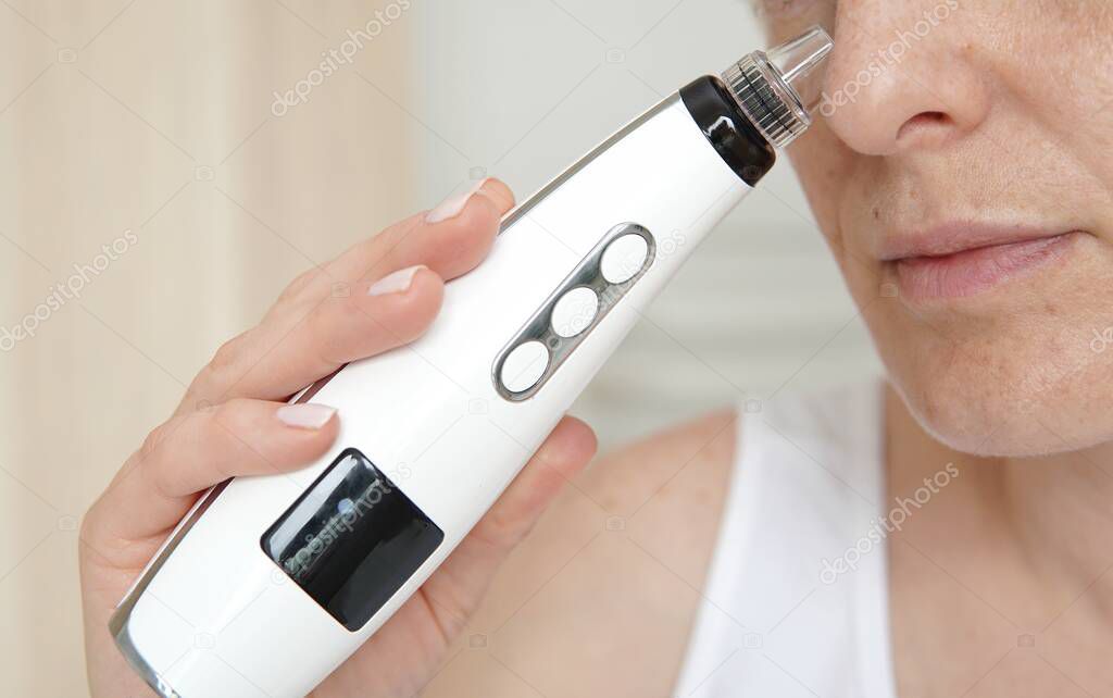 Cosmetic procedure at home, woman cleaning face with vacuum blackhead remover.