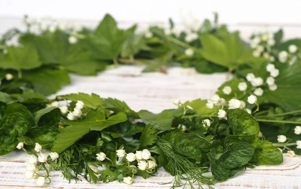Spring collection of medicinal herbs. A wreath of Lily of the valley flowers with other medicinal plants on a wooden white table.
