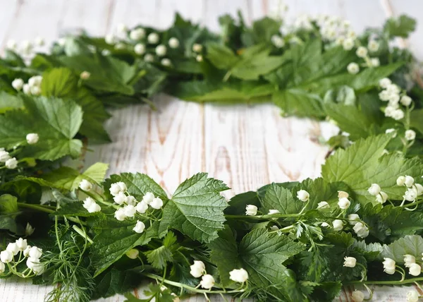 Spring collection of medicinal herbs. A wreath of Lily of the valley flowers with other medicinal plants on a wooden white table.