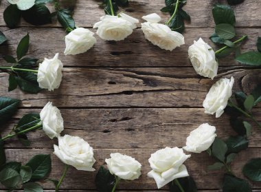 Yukarıdan manzara. Yeşil yapraklı beyaz güller doğal ahşap bir masa üzerinde oval bir şekilde düzenlenir. Çiçek çerçevesi kavramı. Tatil tebriği ya da mesajı.