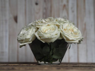 Ön manzara. Beyaz bir buket beyaz gül, beyaz bir ahşap arka planı olan doğal bir ahşap masanın üzerinde duruyor. Bayram selamı ya da kartpostal..