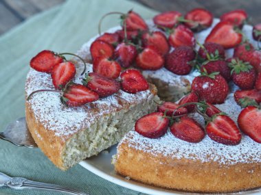 Yakın plan. Böğürtlenli kek üzerine pudra şekeri serpiştirilmiş, yukarıdaki yeşil peçeteye çilek serpiştirilmiş, ahşap arka planda. Ön görünüm.