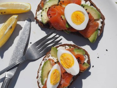 Sağlıklı kahvaltı. Beyaz ahşap arka planda krem peynirli, yumurtalı, avokadolu ve somon balıklı tam tahıllı sandviç. Yukarıdan görüntüle.