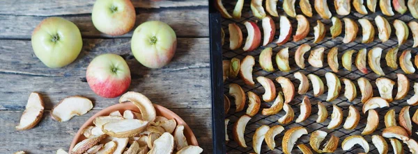Apple chips, fresh apples and dried slices in a rack from the dryer on a wooden background. Homemade dried fruits for future use.