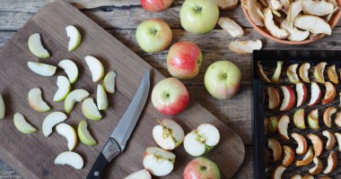 Kurutulmuş meyve toplama mevsimi. Elma cipsi, taze elma ve kurutucudaki kuru dilimler ahşap bir arka planda..
