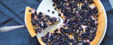 Ev yapımı pişirme. İt üzümü ve elmalı yaz pastası, çırpılmış yumurtalara batırılmış bir fincan çay ve gri ahşap bir masada çatalla. Yukarıdan görüntüle.