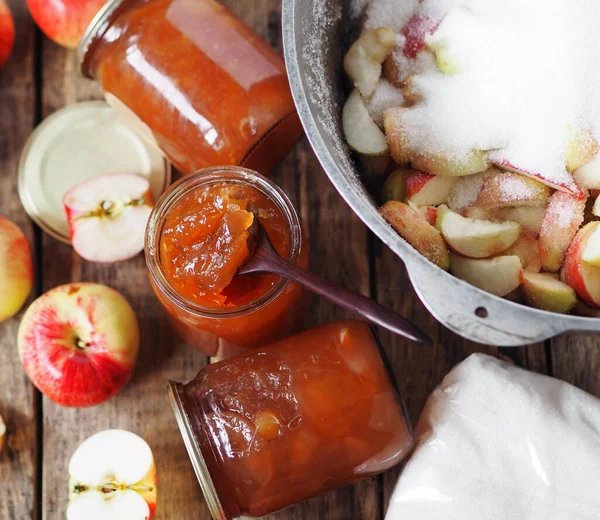 Cook apple jam and close it in jars for future use. Wooden background with apple jam, apples, glass jars and a saucepan with chopped apples. Homemade jam.