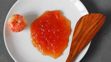 Gri ahşap arka plan, beyaz bir tabakta elma reçeli, bir kaşık ve taze elmalar. Gelecek kullanım için sonbahar ev yapımı reçel.