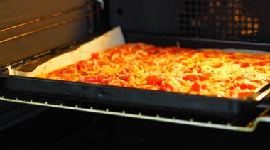 Yemek arkaplanı. Ev yemeği. Domatesli, sosisli ve peynirli pizza, parşömen kağıdının üzerinde fırında pişmiş..