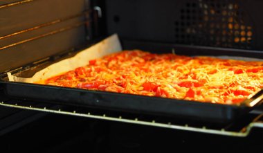Yemek arkaplanı. Ev yemeği. Domatesli, sosisli ve peynirli pizza, parşömen kağıdının üzerinde fırında pişmiş..
