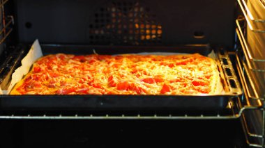 Yemek arkaplanı. Ev yemeği. Domatesli, sosisli ve peynirli pizza, parşömen kağıdının üzerinde fırında pişmiş..