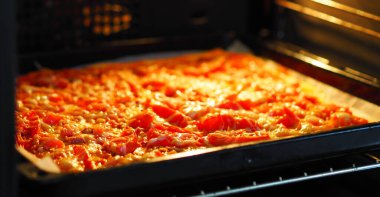 Domatesli, sosisli ve peynirli pizza, parşömen kağıdında fırında pişirilmiş bir kabın içinde. Gıda arkaplanı.