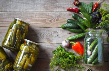 Konserve salatalığın faydaları ve zararları. Kışın depolamak için cam kavanozların altındaki salatalıkları konserveleme işlemi. Ahşap bir arka planda muhafaza için gerekli malzemelerle dolu kavanozlar dolusu salatalık..