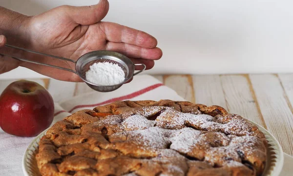 Grandma is homemade cakes Grandma\'s hands sprinkle a round apple pie with powdered sugar.