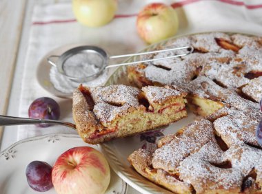 Tahta bir masa üzerinde elmalı ve erikli dilimlenmiş turta. Ev yapımı bisküvi Charlotte, pudra şekerli..